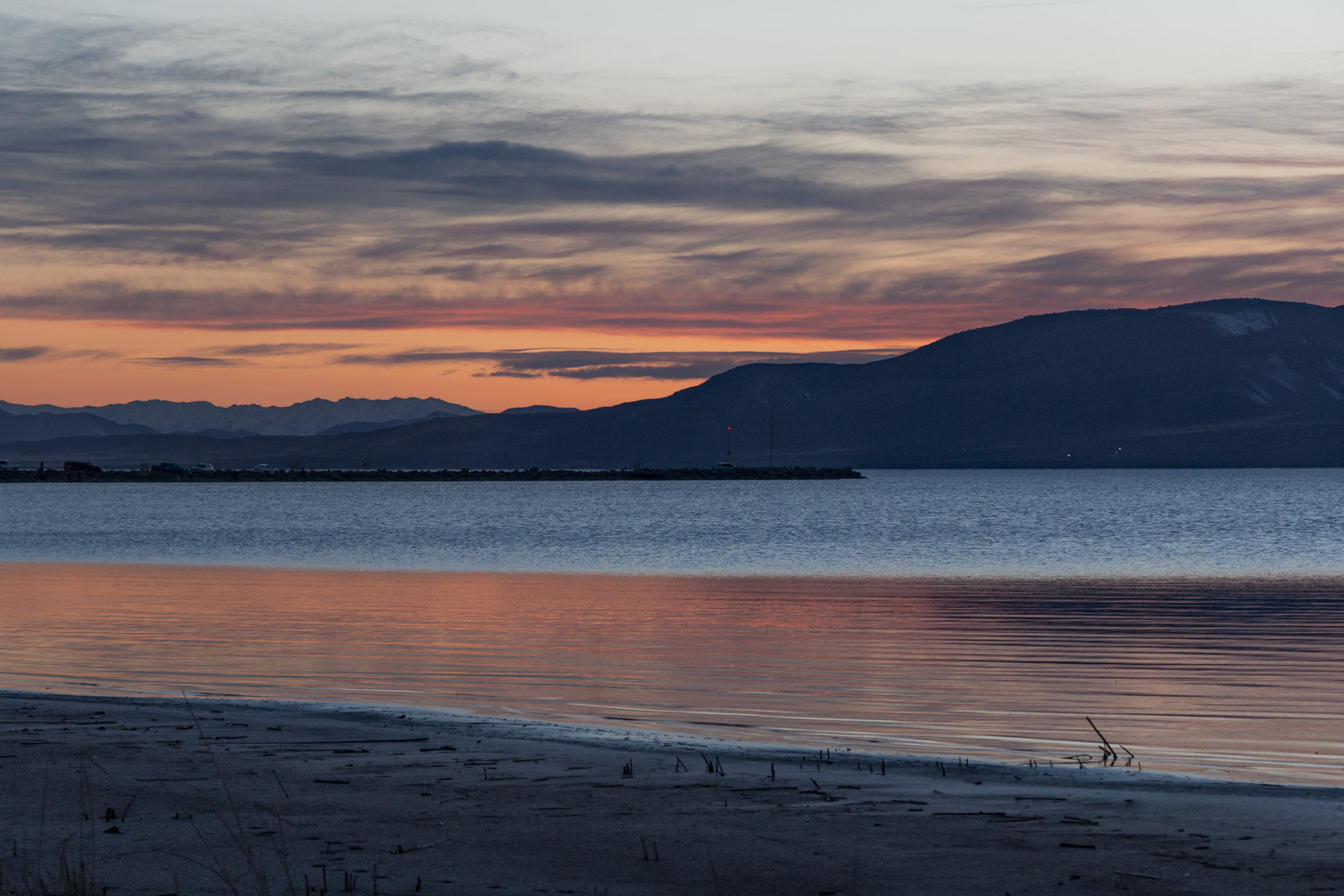 At sunset the further off water reflects the blue sky and the closer calm water reflects the orange sunset sky